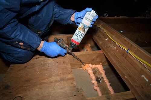 Worker using air sealant in an attic
