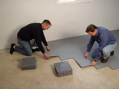 Two contractors installing ThermalDry basement floor matting over a concrete floor