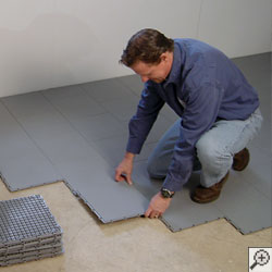 A waterproofing contractor installing waterproof basement subfloor tiles in a basement.