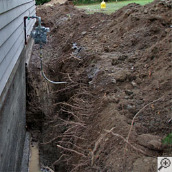 A backhoe excavating dirt from around the edge of a home foundation