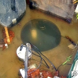 A sump pump can be seen underneath several inches of muddy, dirty water.