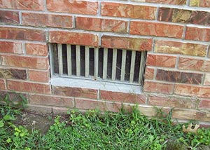 A dirt floor crawl space with a black plastic liner and sagging fiberglass insulation