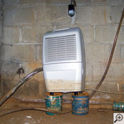 A dehumidifier sitting on two coffee cans, with a mud stain a third of the way up the system from floodwaters.