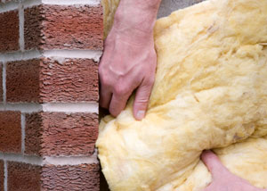 Fiberglass insulation being installed in a basement with brick walls.