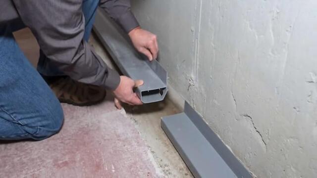 A person installing the WaterGuard drainage system. He is placing the WaterGuard pipe into a trench in the ground.