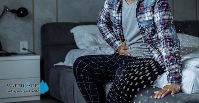 man holding abdomen in pain sitting in bed 