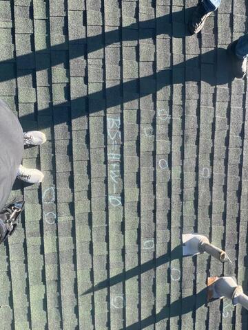 Storm-related hail impact markings on green architectural shingles during residential roof inspection and insurance documentation process.