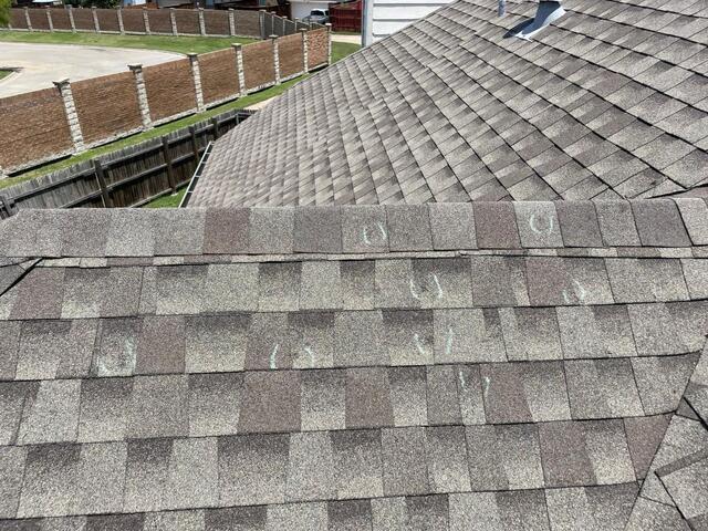 Close-up inspection of hail damage impacts on architectural asphalt shingles during residential roof assessment in Allen, Texas.