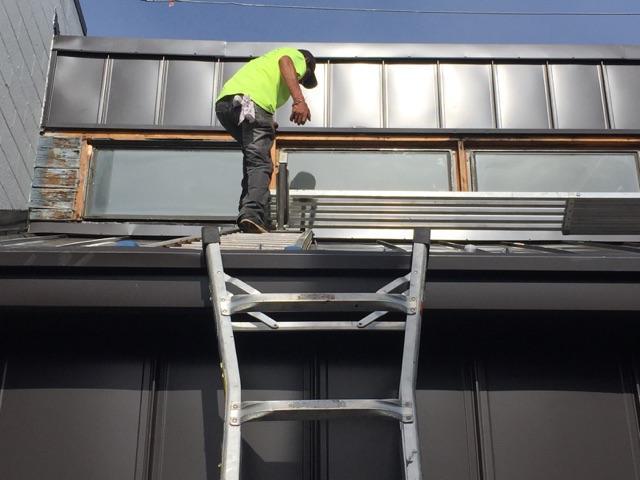 Worker works off pitched metal roof to replace window jambs that were found to be leaking