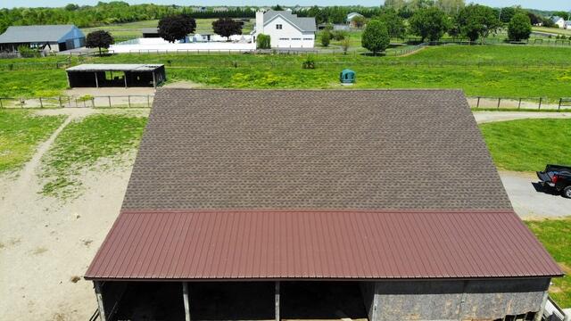 Drone shot showcasing the full barn roof installation, blending architectural asphalt shingles with durable corrugated metal roofing.
