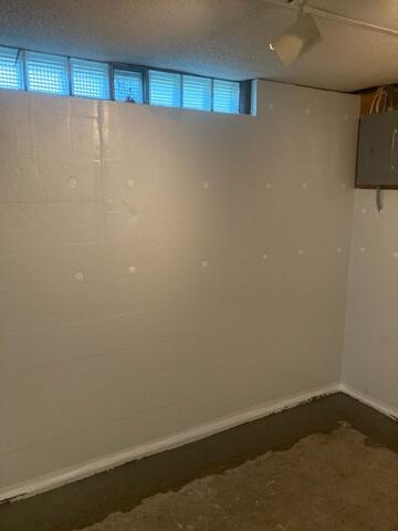 This image shows a basement wall after professional waterproofing work has been completed. The previously exposed concrete block wall is now covered with a CleanSpace vapor barrier, a bright, white, durable liner securely fastened in place. The system helps seal out moisture and directs any water intrusion down into a drainage system at the base of the wall. You can see fresh concrete along the perimeter of the floor, indicating the installation of an interior drainage system like WaterGuard, which is buried beneath the floor and channels water to a sump pump. The space looks much cleaner, brighter, and better protected from future water damage.
