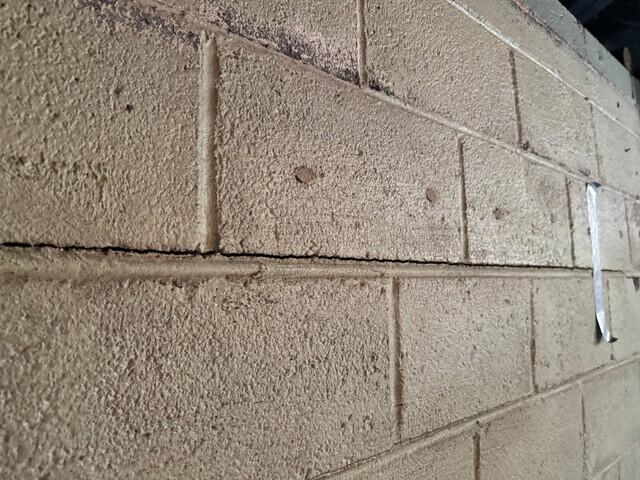 Visible crack and separation in the block wall, showing signs of bowing and structural stress in the basement.