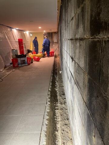 Efflorescense is visible on the cinderblock walls of the home. The process in the photo shows the beginning stages of waterproofing installation.