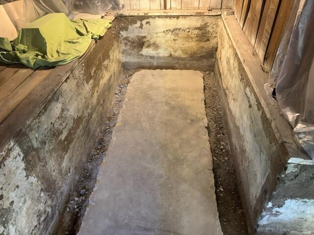 This photo shows an open trench with weep holes drilled into the coves. This trench was dug on top of the footing of the home. Our WaterGuard is always installed on the top of the footing to ensure it stays out of the "mud-zone" found below and next-to the footing. Before jackhammering the floor, we made sure to protect the space from dust with plastic. This included covering the vents and all the homeowners items.