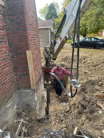 The next step was to drill our piers down into load-bearing strata. The device we use to install them includes pressure gauges that show how much resistance the pier encounters as it's driven into the ground. Once the gauge reaches the target PSI, we know the pier has reached solid, stable soil capable of carrying the structure's weight. You'll also notice that our piers are installed at a slight angle away from the foundation instead of straight down. This angle helps the bracket seat more securely against the bottom of the footing while also providing stronger overall support against the weight and outward pressure of the foundation.