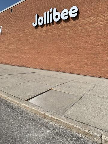Pre-repair assessment of a sunken concrete slab at a commercial storefront. Significant soil settlement has caused a deep vertical offset between panels, creating a hazardous tripping point for pedestrians.