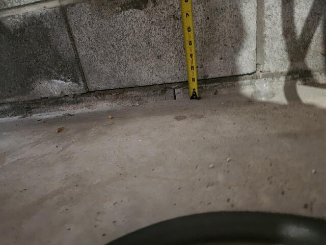 A tape measure confirms a one-inch gap between the garage floor and the foundation wall. This vertical shift proves the slab has lost its sub-surface support and is actively sinking away from the main structure.