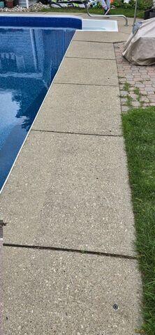 Uneven concrete along the pool edge showing visible settlement and separation between slabs, creating trip hazards and improper drainage around the pool deck.