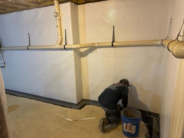 Our crew installing the WaterGuard drainage system along the basement perimeter to capture and redirect water away from the foundation.