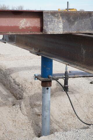 Helical piers installed and aligned beneath structural steel, ready to transfer load to competent bearing soils approximately 75 feet below grade. Torque-monitored installation verified capacity for each production pier.