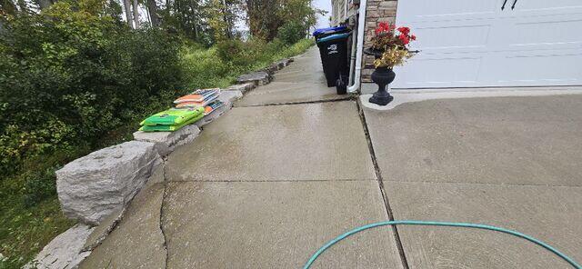 Water from the downspout pooled at the garage corner, washing away the sub-base and causing the concrete slabs to sink. This created an uneven surface and a serious trip hazard, highlighting the need for professional concrete leveling.