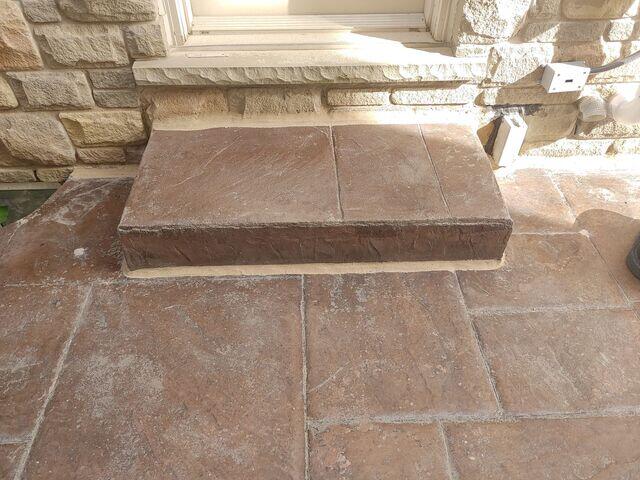 A close-up of the stamped concrete side entrance step. Previously a major tripping hazard, the step has been precision-lifted back to its original position using polyurethane injection. The fresh sealant around the base and top joints ensures a seamless, safe transition for anyone entering or exiting the home.