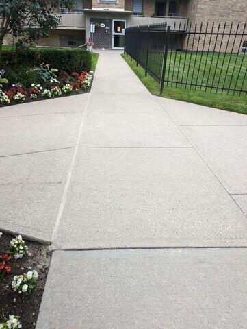The primary sidewalk leading to the building's entrance. The restoration created a flat, continuous surface that is essential for residents using mobility aids or strollers, ensuring that the main access point is both welcoming and secure.