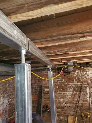 The crew sistered the weakened floor joists in the basement before installing a supplemental steel beam and SmartJacks.