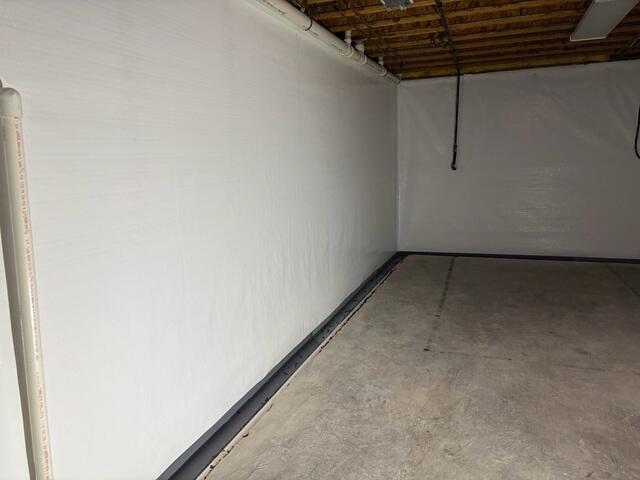 A clean unfinished basement with freshly installed CleanSpace® bright white wall vapor barrier covering the foundation walls and a discreet WaterGuard® drainage system installed along the perimeter edge of the basement floor. The space looks dry, protected, and professionally waterproofed, with a neat appearance and improved moisture control throughout the basement.