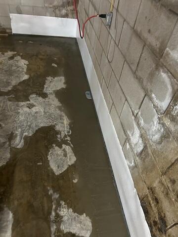 The crew installs WaterGuard around the basement perimeter to drain wall leaks.