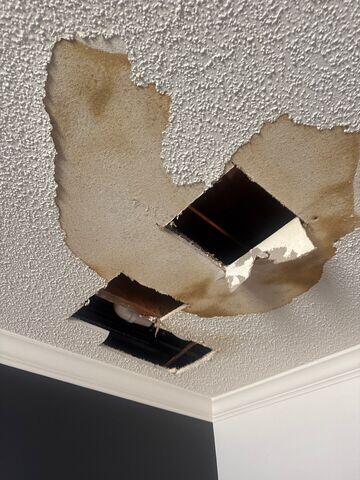Close-up of the ceiling damage showing missing drywall and popcorn texture around the repair areas.