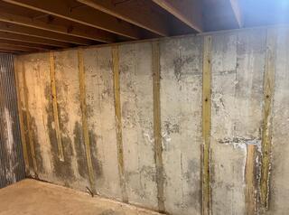 A full photo of the compromised basement wall, with everything moved out of the way it is clear to see it bowing inward.