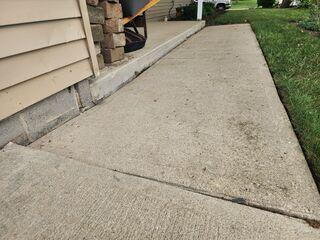 This photo shows the sidewalk that connects the driveway to the front porch. We injected Polylevel foam into the slabs to raise and level the sidewalk back out. PolyLevel foam is a lightweight, fast-curing polyurethane material that is injected beneath concrete slabs to lift and level uneven surfaces. It expands to fill voids, stabilizes the soil, and prevents future settling, making it an ideal solution for driveways, patios, sidewalks, and other sunken concrete areas. Check out the next photo to see this section lifted and sealed.