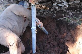 Justin drives a Helical Pier deep into the ground to reach stable, load-bearing soil. These steel piers transfer the cabin's weight away from weak surface soils, preventing further settlement and reinforcing the foundation's strength.