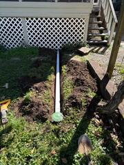 Discharge line exposed during installation, showing the pop-up outlet before final backfilling.