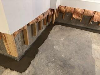 This photo shows the completed subfloor drainage system sealed beneath a smooth layer of concrete. Our WaterGuard drains feature a wall flange that captures any moisture running down the foundation walls and directs it into the drainage channel below. Once the concrete cured, we returned to install the EverLast wall panels.