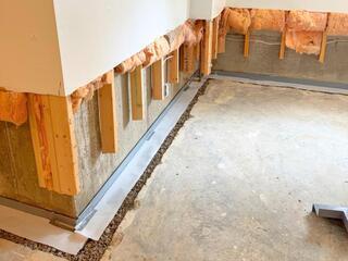 This photo shows the same wall during the waterproofing process. By this point we had removed the drywall, cut the studs,  trenched the perimeter of the floor, fitted the trenches with our WaterGuard subfloor drains, and pitched the drains towards the sump pump.