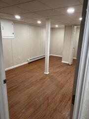 The main living area of the remodeled basement - spacious, bright, and ready to use. Fresh wall panels, a drop ceiling with recessed lighting, and wood-look floors give the room a warm, inviting atmosphere.