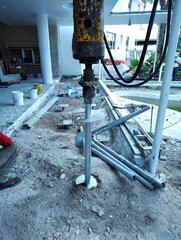 Installing helical piles near Coy Pond with studded new construction brackets installed in the background.