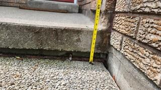 This shot quantifies the structural failure, using a measuring tape to show the 3-inch drop where the slab pulled away from the landing. This gap confirms the significant trip hazard and the void left by eroded soil.