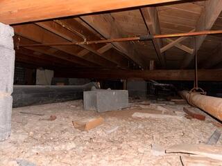 Low-clearance crawl space with exposed areas, damaged screening, and signs of moisture, contributing to structural and environmental concerns.