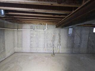 Unfinished basement showing vertical wall cracks, moisture staining, and signs of damp conditions contributing to a musty smell.