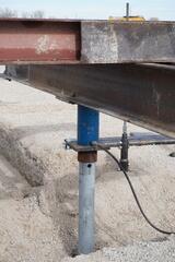 Helical piers installed and aligned beneath structural steel, ready to transfer load to competent bearing soils approximately 75 feet below grade. Torque-monitored installation verified capacity for each production pier.