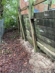 Old, rotten, and wooden fence, no longer able to support the weight of the downward sloping soil.