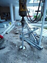 Installing helical piles near Coy Pond with studded new construction brackets installed in background