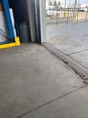 Severe spalling and jagged cracks at the bay door transition, creating a major trip hazard and a jarring "thump" for forklifts.