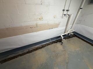 The crew installs the WaterGuard drainage pipe and CleanSpace wall vapor barrier.