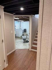 The finished basement provides a bright, comfortable space for relaxing and entertaining, while maintaining easy access to the home's functional areas. Through the doorway, you can see the separate unfinished laundry room, thoughtfully preserved to keep utilities organized and distinct from the newly finished living space.