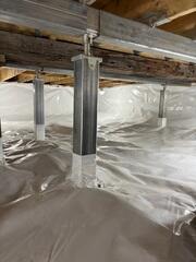 The SmartJack system combines steel support beams, adjustable galvanized steel posts, and engineered bases to stabilize weakened crawl space floor systems. The beams distribute the structural load, while the posts transfer the weight down to stable support locations below.