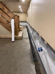 A below-floor interior drainage system is installed around the basement perimeter to capture water and direct it toward the sump pump system.